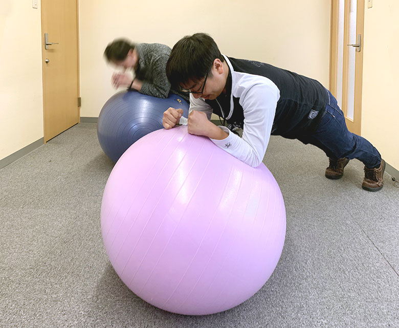 バランスボールを使ってプランクに挑む2名の男性社員